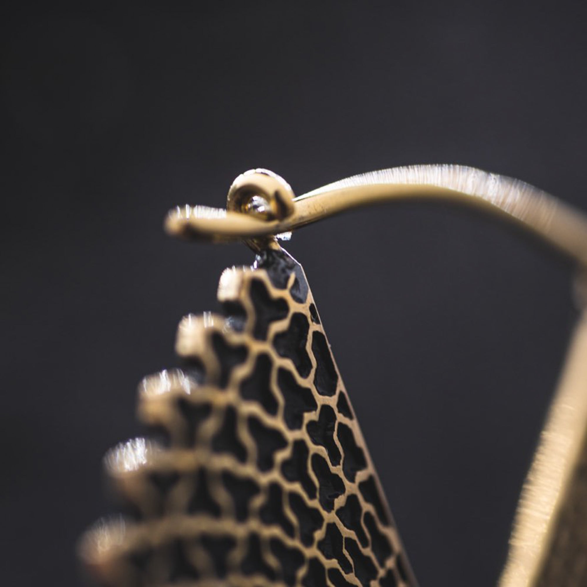 Close-up of a gold VORTEX Tribal Oversized Mandala Disc Hoop Earring by Kaya Movement with an intricate, cut-out design on a black background. The earring features a hook clasp, and the delicate, detailed texture captures the charm of boho statement earrings.
